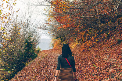 Rear view of woman walking on autumn leaves in forest