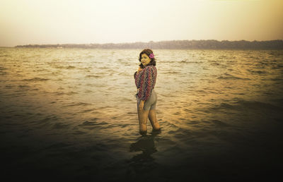 Woman standing on beach against sky during sunset