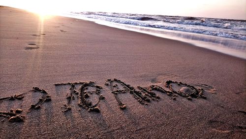 Text on sand at beach against sky during sunset