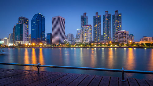 Illuminated city at waterfront against blue sky