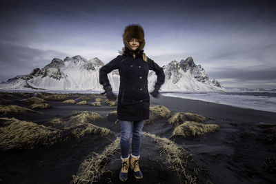 Full length portrait of woman standing on snow covered mountain against sky