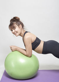 Woman exercising with green fitness ball against white background