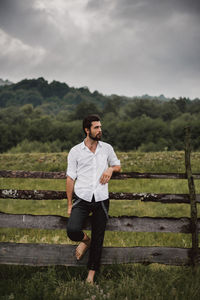 Full length of young man standing by fence on field