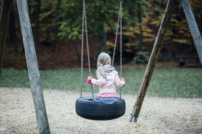Rear view of girl sitting on tire swing at playground