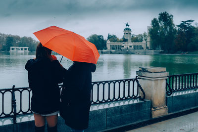 Rear view of man with umbrella standing on railing in river