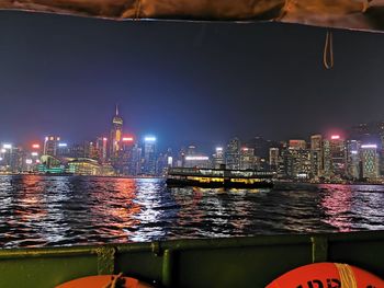 Illuminated buildings by river against sky in city at night