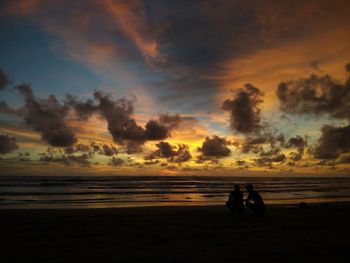 Silhouette people sitting at beach against sky during sunset