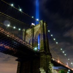 Low angle view of illuminated brooklyn bridge against light beams sky at night