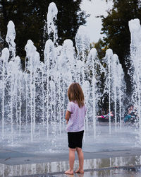 Little girl watching the water play in the summer park