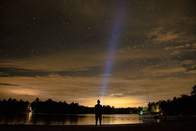 Rear view of silhouette man standing at lakeshore against star field