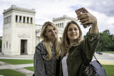 Young woman taking selfie with friend against built structure