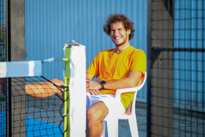 Portrait of young man sitting on chair at tennis court