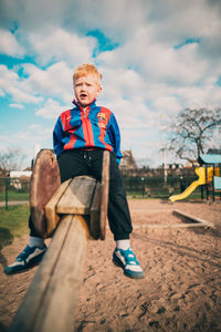 Boy sitting on slide at playground against sky