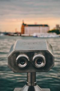 Close-up of coin-operated binoculars against bay during sunset