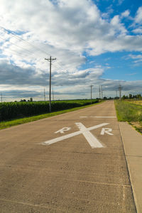 High angle view of railroad crossing sign on road against cloudy sky during sunny day