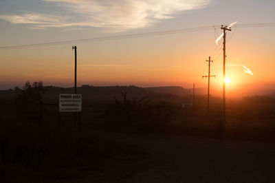 Road sign on silhouette landscape against sky during sunset