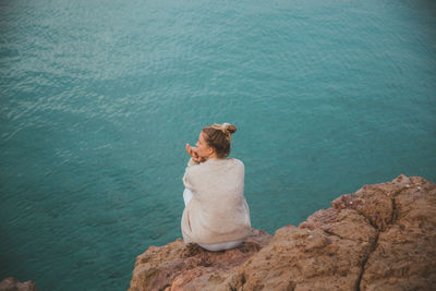 Rear view of man sitting on rock by sea