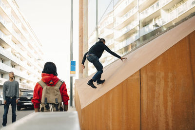 Friends looking at carefree teenage boy climbing on wall in city