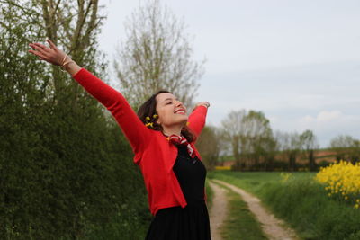 Smiling woman standing with arms raised against plants