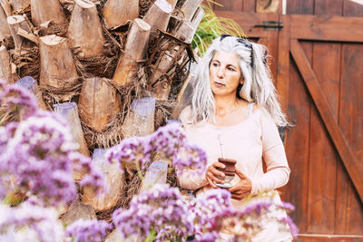 Woman looking away while standing against wooden gate