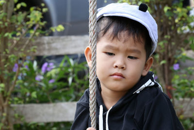 Close-up of cute boy looking away while sitting on rope swing