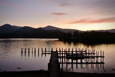 Silhouette wooden posts in lake against sky during sunset