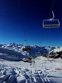 Ski lifts over snow covered landscape against clear blue sky