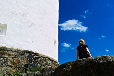 Rear view of woman standing on rock against blue sky