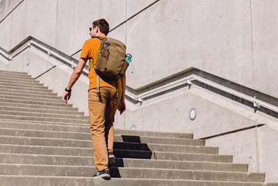 Young man with a backpack going up the stairs on sunny summer day. urban lifestyle