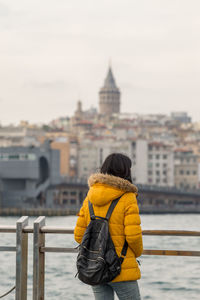 Rear view of woman standing by river with galata tower in background