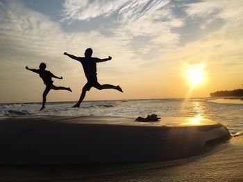 Silhouette men in sea against sky during sunset