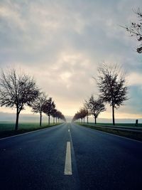 Empty road by bare trees against sky