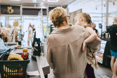 Grandmother carrying granddaughter while standing at checkout counter in supermarket