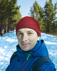 Man smiles in blue jacket and red cap in winter outside