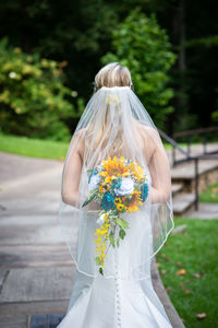 Rear view of bride holding bouquet while standing outdoors