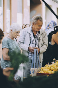 Senior tourist couple shopping for lemons at street market in city