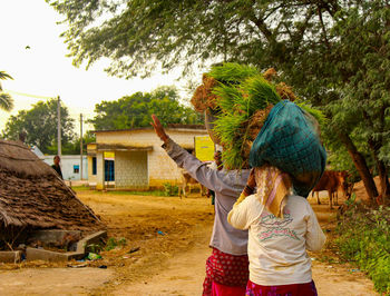 Rear view of women carrying crops on dirt road