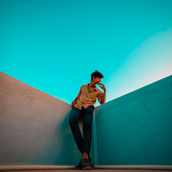 Man standing on wall against clear blue sky