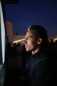 Man looking away while standing outdoors at night