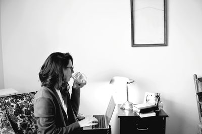 Woman drinking coffee while using laptop at home