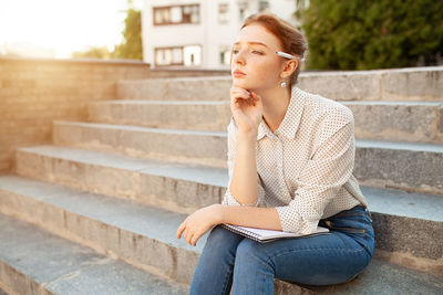 Woman holding book while sitting on steps