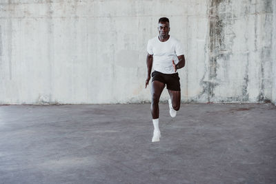 Serious male athlete jumping against white wall