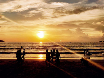 Silhouette people on beach against sky during sunset
