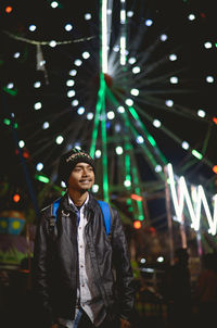 Portrait of young man standing against illuminated lights at night