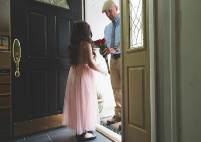 Father giving roses to daughter wearing pink dress at doorway