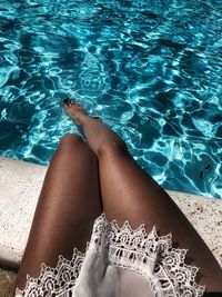 Low section of woman sitting on retaining wall over swimming pool