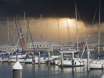 Sailboats moored in harbor at sunset