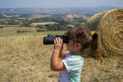 Rear view of woman photographing through binoculars at farm