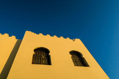 Low angle view of yellow building against clear blue sky