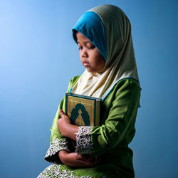 Side view of cute girl holding koran standing against blue background